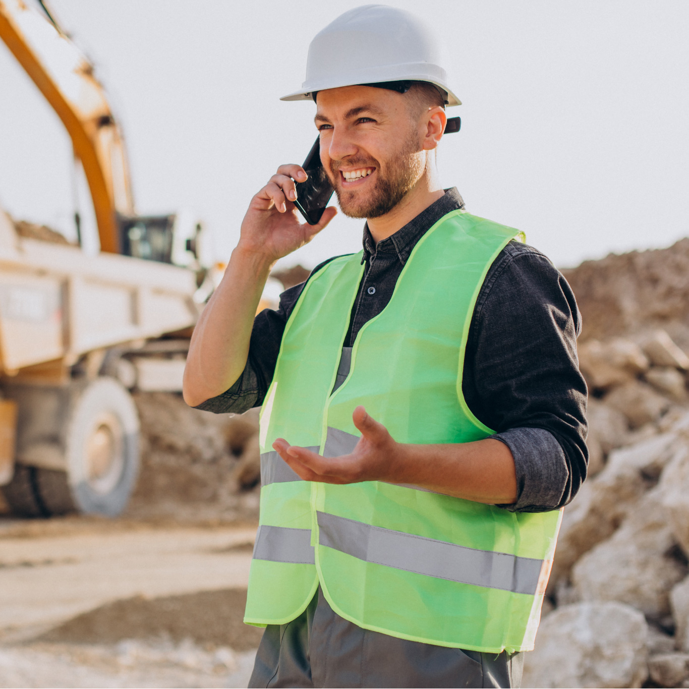 Man on a construction site wearing a hard hat and high vis while on the phone