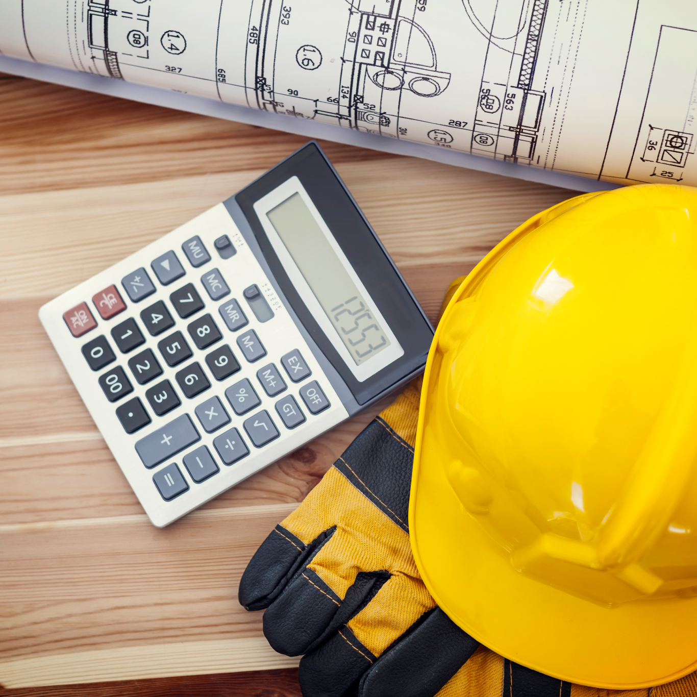 Photo of a hard hat and calculator on a desk next to some plans
