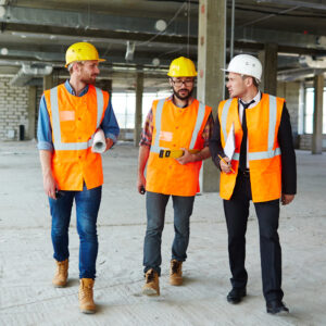 Photo of three men wearing hard hats and high vis walking and talking on a construction site