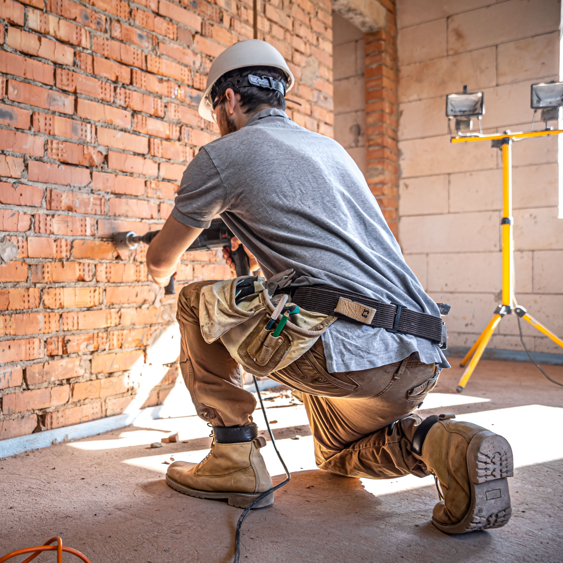 Male construction worker wearing a hard hat and drilling into a wall