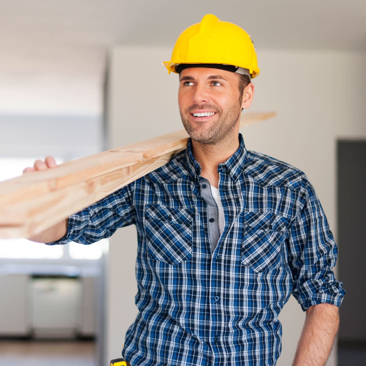 male construction worker holding planks of wood in yellow hard hat