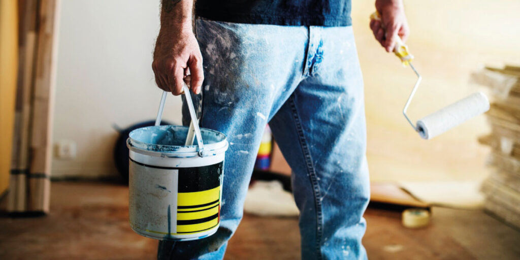 Photo of a man holding a paint bucket and paint roller