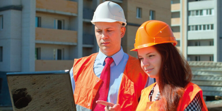 Photo of two construction workers wearing PPE and looking at a laptop screen