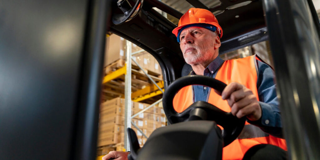 A factory worker servicing a forklift truck, with safety equipment visible.