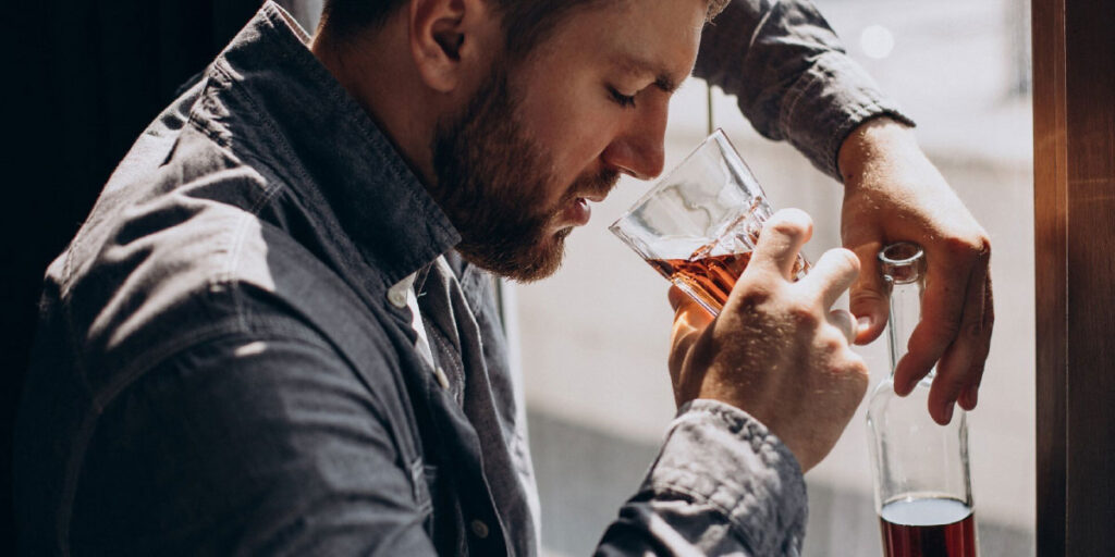 Photo of a man drinking an alcoholic beverage from a glass while holding the bottle in the other hand