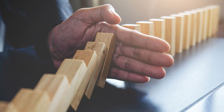 Photo of dominos falling while a man places his hand between them to stop them falling any further