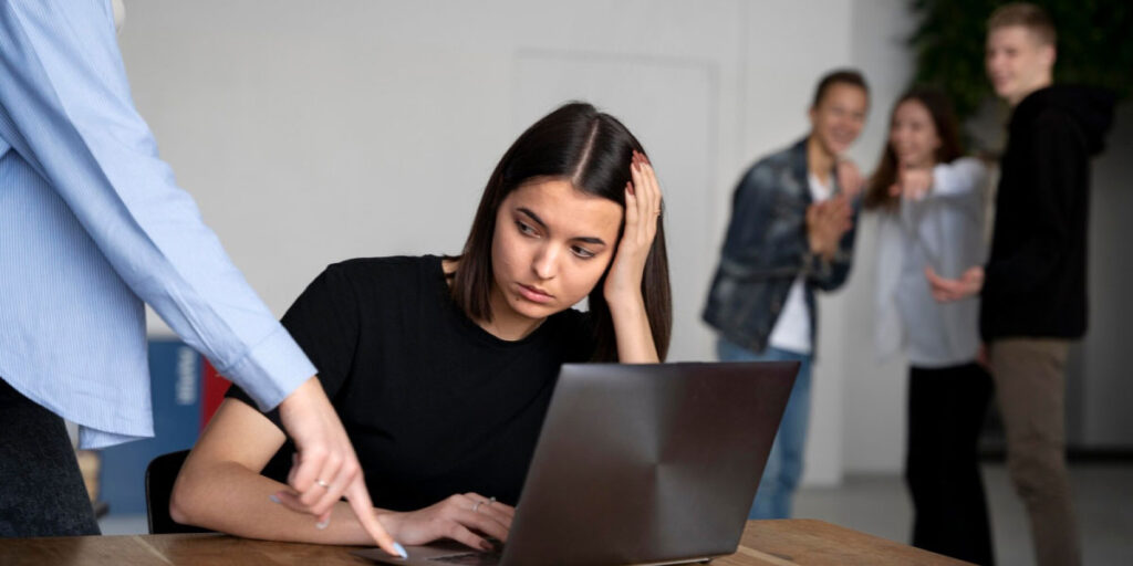 Photo of a sad looking worker being disciplined while people behind her laugh and point in her direction