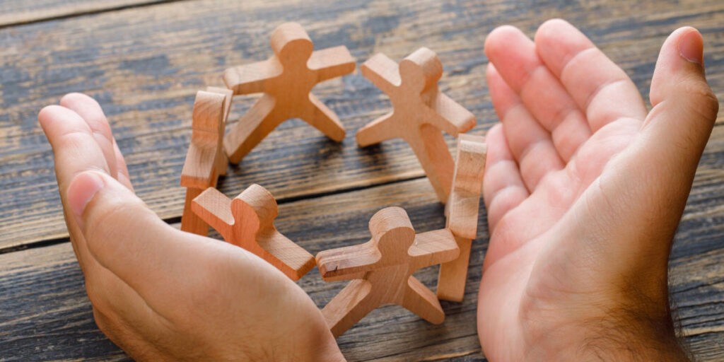 Photo of small wooden figurines in a circle while two hands are placed on either side in a protective fashion