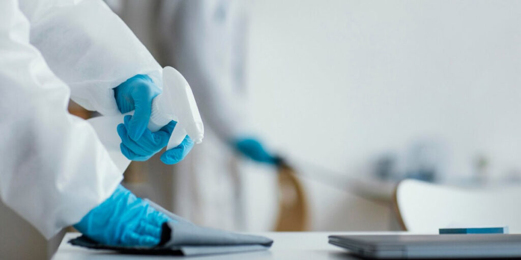 Photo of a worker cleaning an office desk while wearing PPE