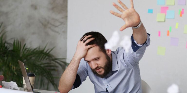 Photo of a stressed looking worker throwing crumpled up paper into the air