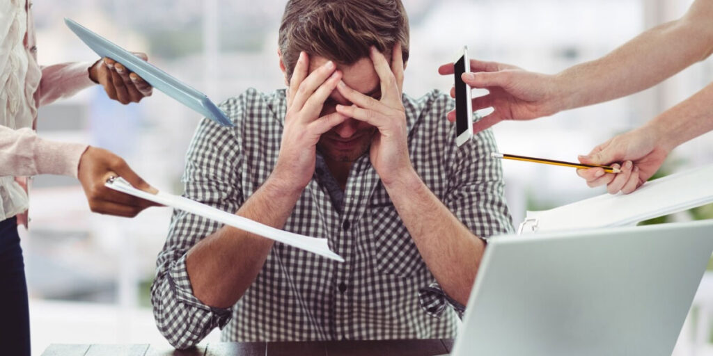 Photo of a stressed worker being passed documents by multiple employees