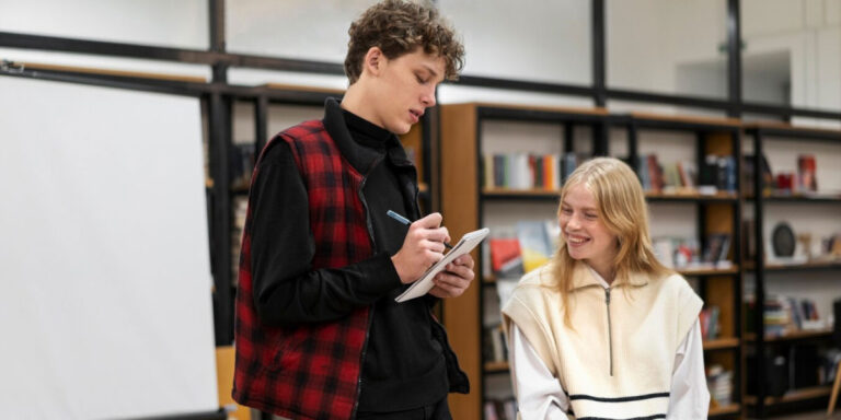 Photo of two young people speaking while one writes notes on a notepad