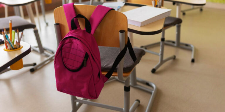 Photo of a desk and chair in a classroom with a bag on the back of the chair