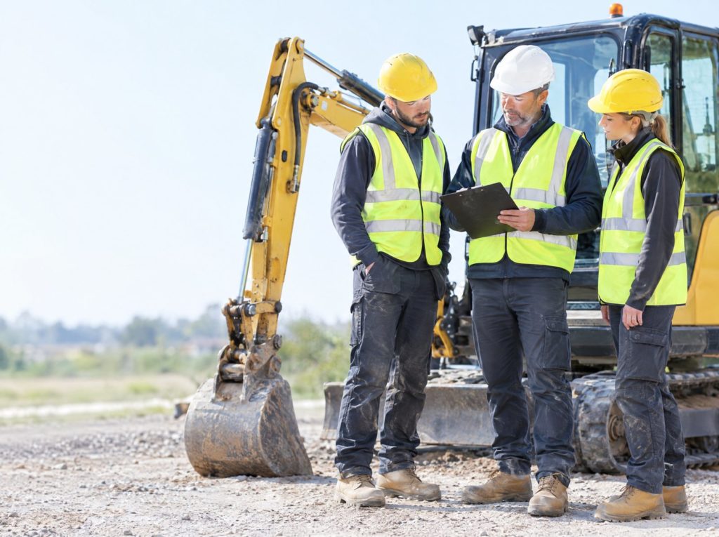 Groundworks supervisor checking a clipboard with two operatives beside a mini excavator